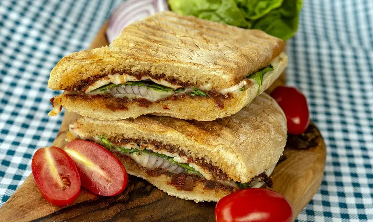 Pyszne panini z kurczakiem, suszonymi pomidorami i serem, podane z pomidorkami koktajlowymi i sałatą.