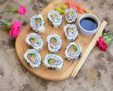 Pyszne california sushi z łososiem i awokado, podane na desce z różowymi kwiatami i pałeczkami.