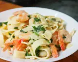 Makaron tagliatelle z krewetkami i zielonymi ziołami w kremowym sosie na białym talerzu.