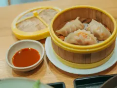Parujące pierogi gyoza w bambusowym parowniku, obok miseczka z sosem.