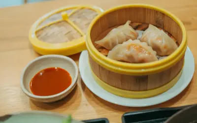 Parujące pierogi gyoza w bambusowym parowniku, obok miseczka z sosem.