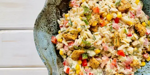 Pyszna sałatka z makaronem orzo i kurczakiem, z dodatkiem kukurydzy, papryki i ziół, podana w ceramicznej misie.