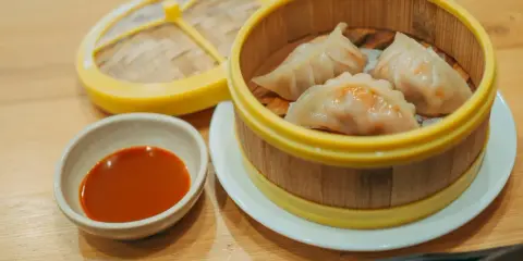 Parujące pierogi gyoza w bambusowym parowniku, obok miseczka z sosem.