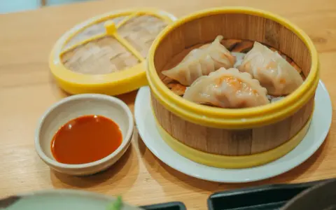Parujące pierogi gyoza w bambusowym parowniku, obok miseczka z sosem.