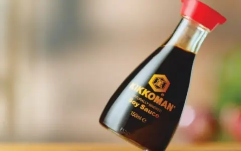 Butelka sosu sojowego Kikkoman z czerwoną zakrętką na drewnianym blacie.
