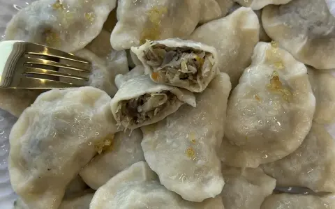 Talerz pełen pysznych, domowych pierogów z kapustą i grzybami. Jeden pieróg jest przekrojony, ukazując bogate nadzienie. Obok leży złoty widelec.