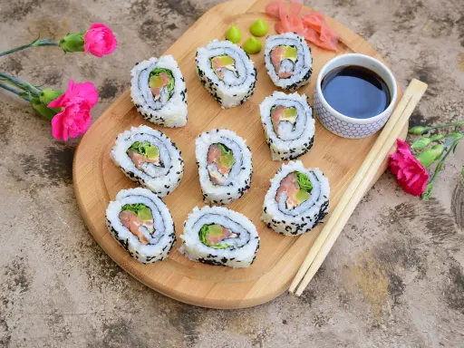 Pyszne california sushi z łososiem i awokado, podane na desce z różowymi kwiatami i pałeczkami.