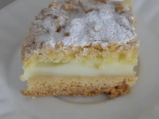 Kawałek ekspresowego kruchego ciasta z budyniem, posypana cukrem pudrem. Idealne na szybką przekąskę.