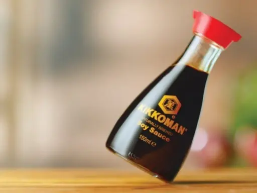 Butelka sosu sojowego Kikkoman z czerwoną zakrętką na drewnianym blacie.