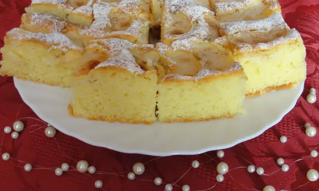 Puszyste ciasto z owocami na oleju i kruszonką, posypane cukrem pudrem, prezentuje się apetycznie na białym talerzu.
