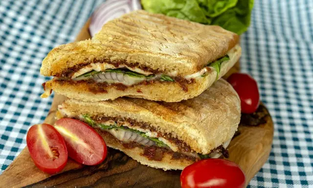 Pyszne panini z kurczakiem, suszonymi pomidorami i serem, podane z pomidorkami koktajlowymi i sałatą.