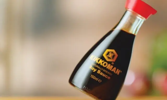 Butelka sosu sojowego Kikkoman z czerwoną zakrętką na drewnianym blacie.