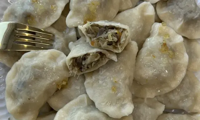 Talerz pełen pysznych, domowych pierogów z kapustą i grzybami. Jeden pieróg jest przekrojony, ukazując bogate nadzienie. Obok leży złoty widelec.