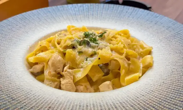 Pyszny makaron włoski z kawałkami kurczaka w kremowym sosie, posypany ziołami i parmezanem.