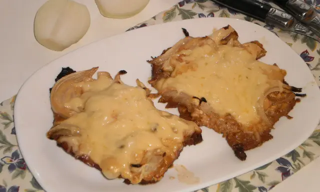 Pyszny schab w cebuli, zapieczony z serem, idealny na niedzielny obiad. Obok leżą połówki cebuli.