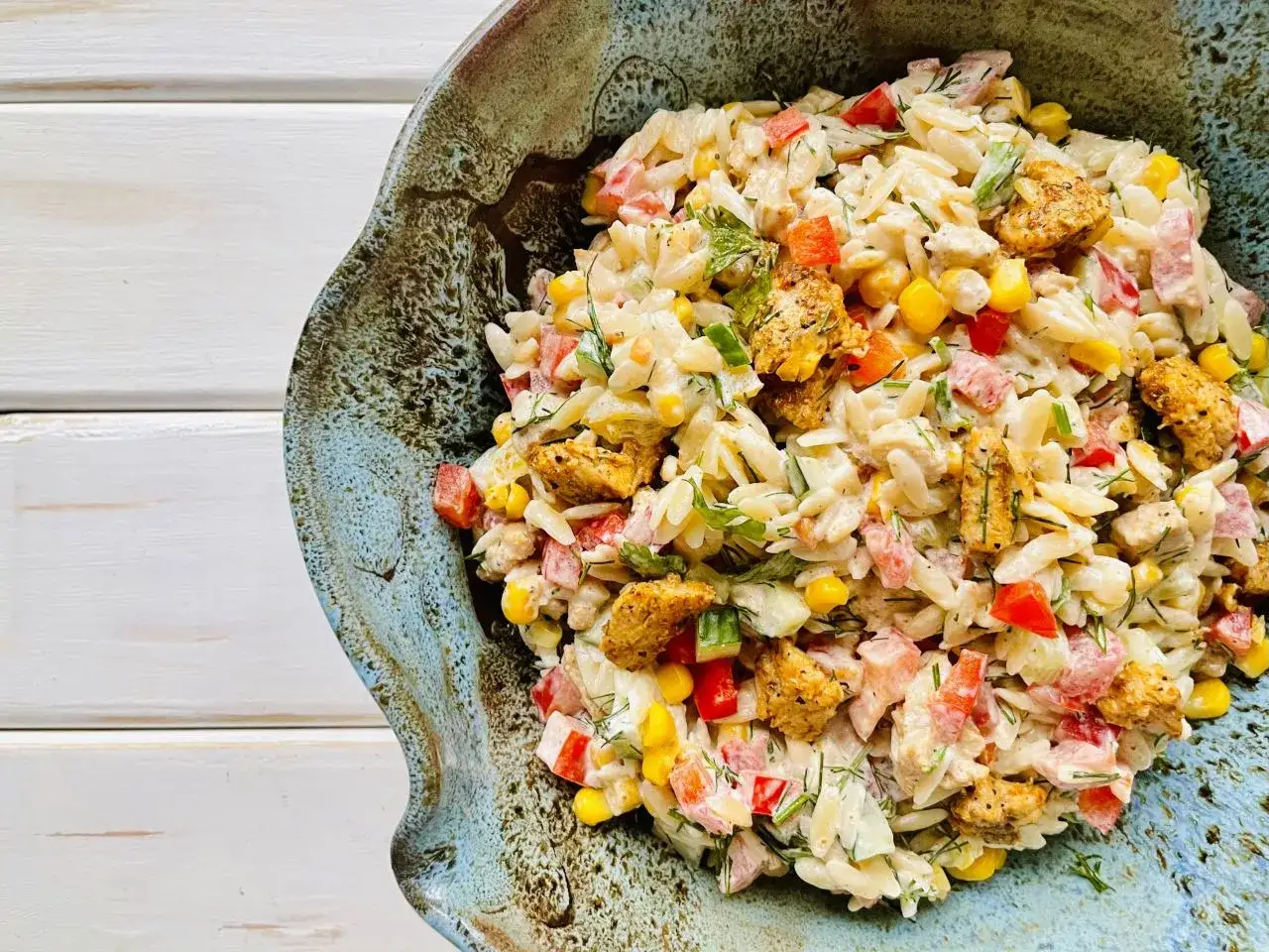 Pyszna sałatka z makaronem orzo i kurczakiem, z dodatkiem kukurydzy, papryki i ziół, podana w ozdobnej misie.