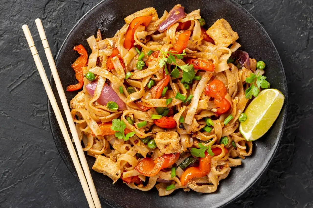 Pad Thai z kurczakiem na talerzu, widok z g&oacute;ry, z limonką i orzeszkami